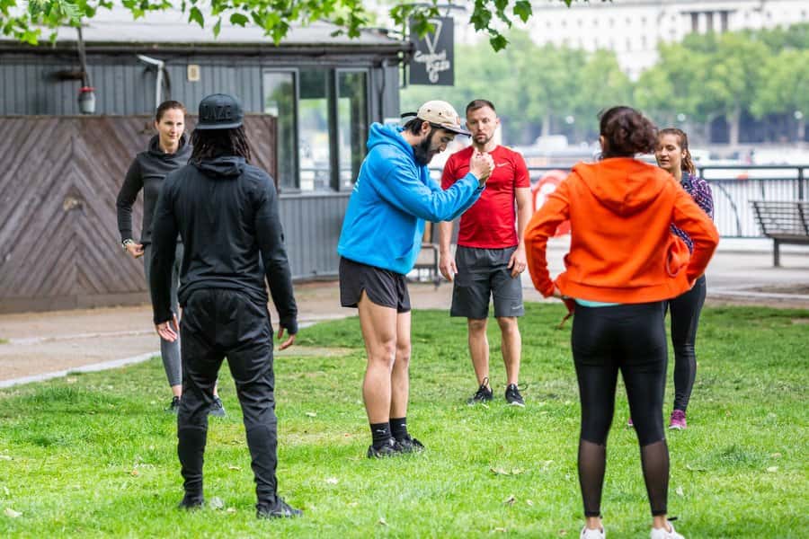 A group of people outdoors receiving instruction from a personal trainer.